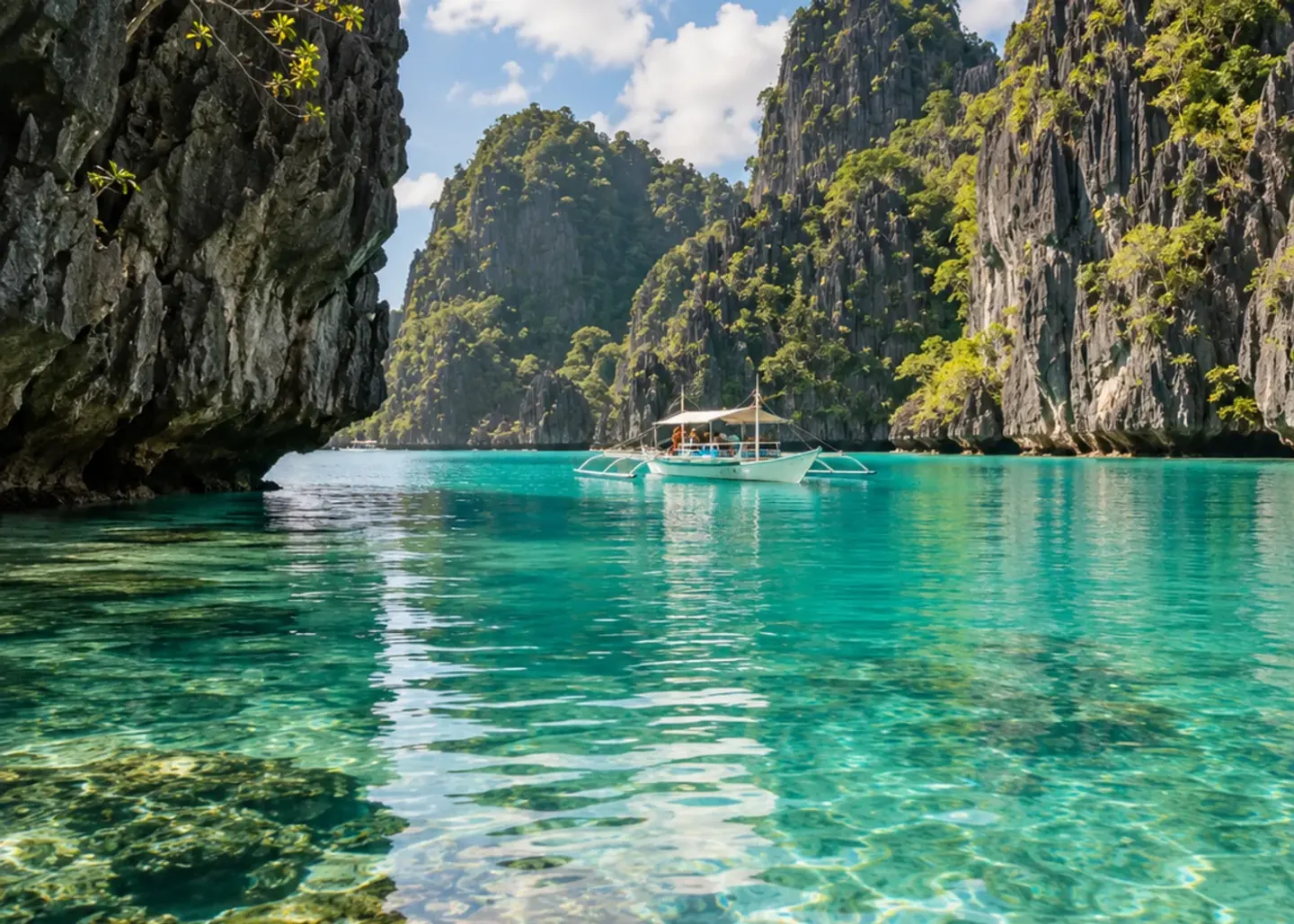 A small outrigger boat beneath limestone cliffs in turquoise water.